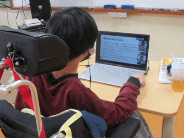 車椅子に座った小学生の男の子が熱心にパソコンに向かう写真